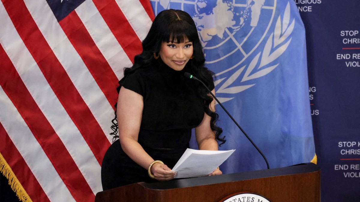 Imaginea surprinde o artistă vorbind de la un pupitru oficial, având în față un document, într-un cadru instituțional. În fundal se văd steagul Statelor Unite și simbolurile Organizației Națiunilor Unite, sugerând un eveniment cu caracter oficial sau diplomatic.