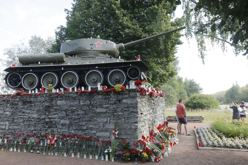Oameni pozându-se lângă tancil sovietic T-34 care comemora eliberarea țării de sub Germania nazistă de către Uniunea Sovietică, în timpul celui de-Al Doilea Război Mondial, în orașul Narva, Estonia | Foto: Hepta