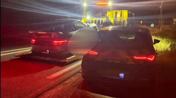 O mașină pe care scrie Gendarmerie oprită pe marginea drumului lângă o platformă de tractare pe care se află o mașină neagră