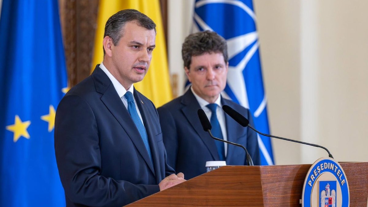 Eugen Tomac, îmbrăcat în costum negru și cravată albastră, la Palatul Cotroceni, și Nicușor Dan, președintele României, îmbrăcat în costum și cravată albastră, iar pe fundal steagurile României, UE și NATO