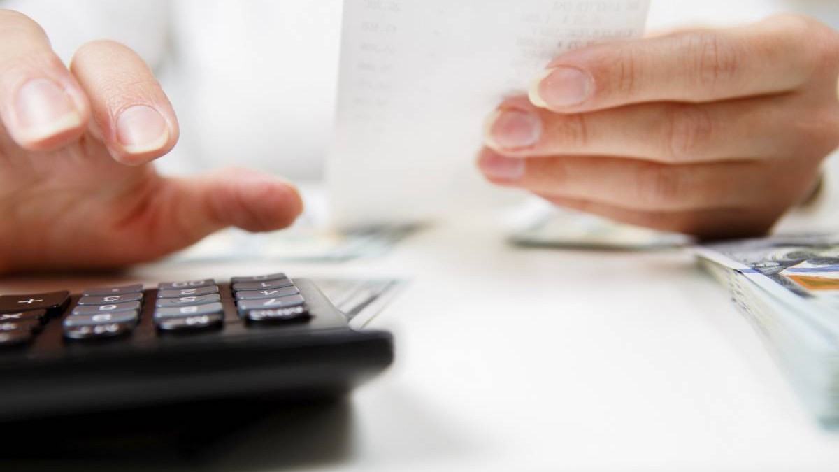 prim-plan cu mâini cu calculator care numără bani și își iau notițe acasă. Conceptul de economii