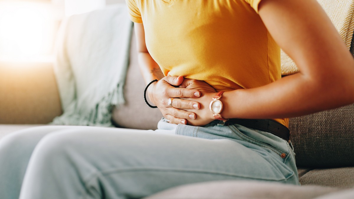 Femeie, sta pe canapea si se tine cu mainile de abdomen