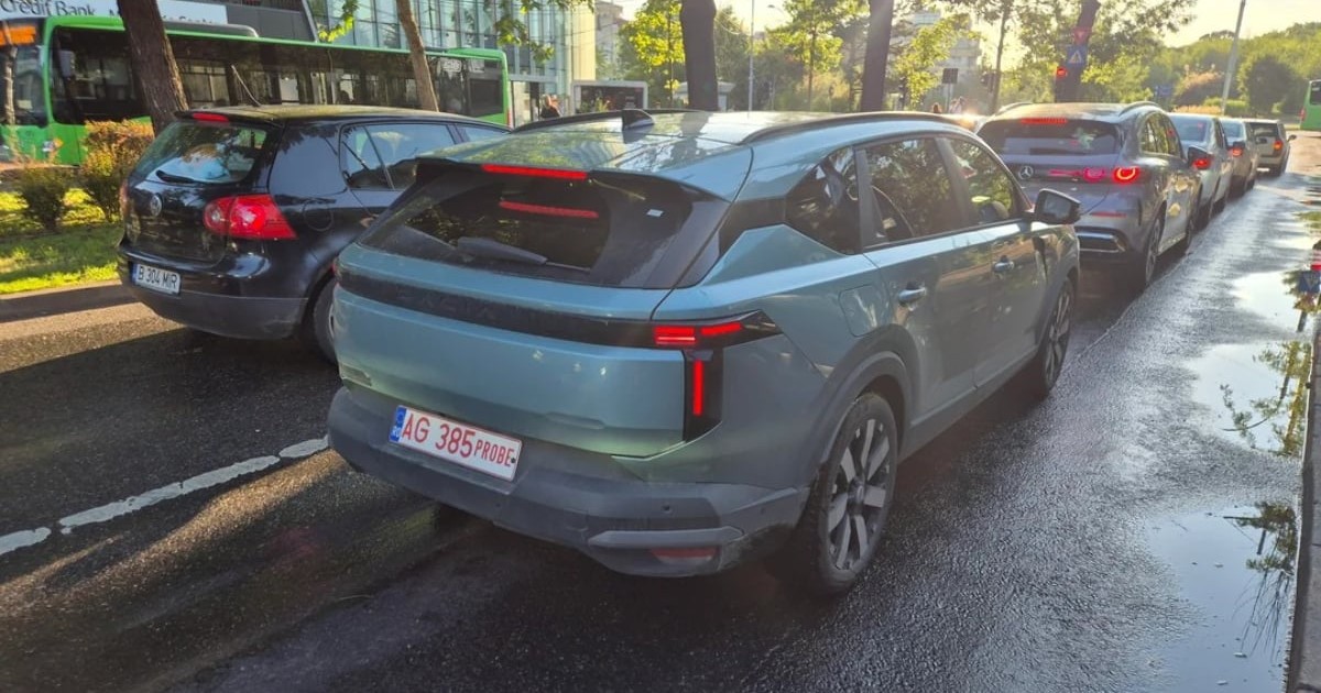 Imaginea surprinde noua Dacia Striker în trafic, pe o stradă din București, având numere provizorii de test și un design de tip crossover cu plafon coborât spre partea din spate. Se remarcă stopurile LED verticale și silueta robustă a mașinii, fotografiată în timpul testelor înainte de lansarea oficială pe piață.
