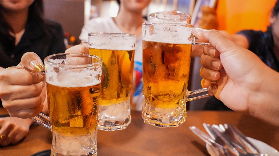 Imaginea surprinde mai multe persoane ciocnind halbe cu bere într-un local, într-o atmosferă relaxată și convivială. Paharele pline cu bere sunt ridicate pentru un toast, sugerând un moment de socializare între prieteni.