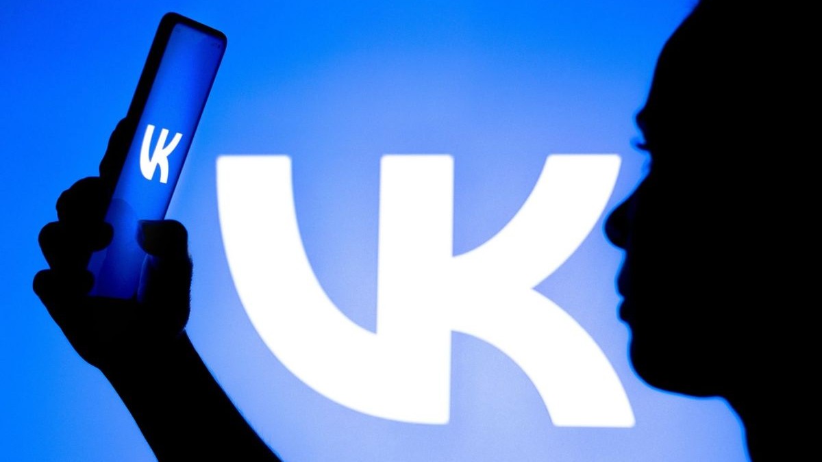 Silueta unei femei care ține în mână un smartphone cu sigla VKontakte (VK) afișată pe ecran și în fundalul care este albastru, Brazilia, 23 martie 2022