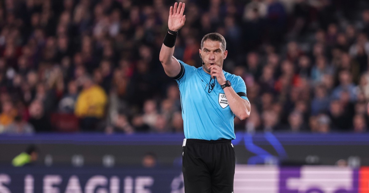 Istvan Kovacs pe terenul de fotbal cu un tricou albastru și pantaloni scurți negri. Acesta fluieră și ține mâna dreaptă sus.