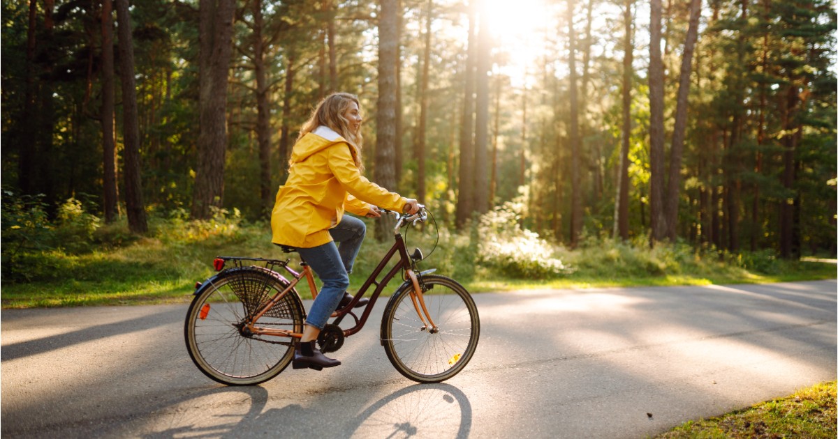 O femeie îmbrăcată cu geacă galbenă, pe o bicicletă, care se plimbă într-un parc