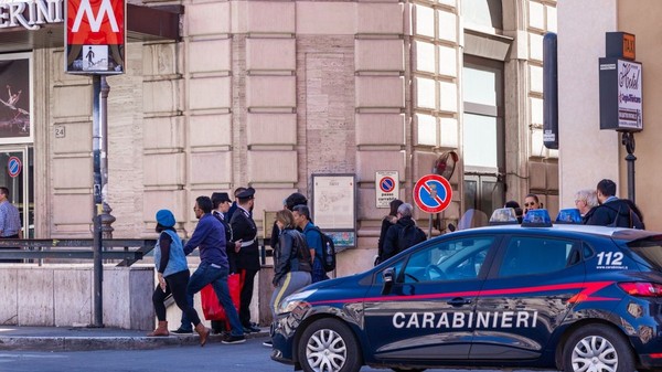 O mașină de Carabinieri oprită în dreptul unei stații de metrou din Milano, mai mulți turiști în haine groase coboară pe scările de la metrou