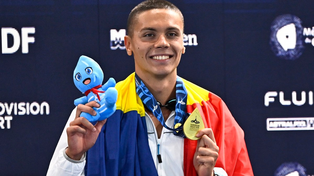 David Popovici ține steagul tricolor pe podiumul de premiere, după ce a cucerit aurul în proba de 100 metri la Campionatul european de laParis, 12 august 2026