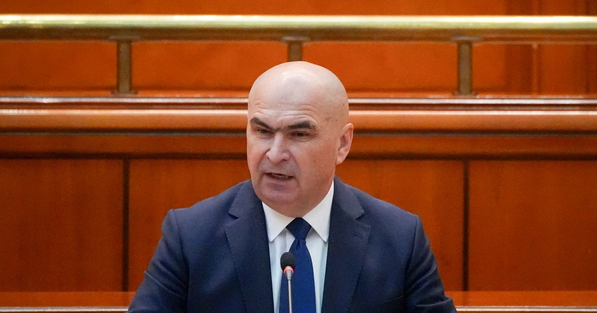 Ilie Bolojan surprins în timp ce vorbește la microfon la Palatul Parlamentului, în iunie 2025. Poartă un sacou albastru închis, o cravată de aceeași culoare și o cămașă albă