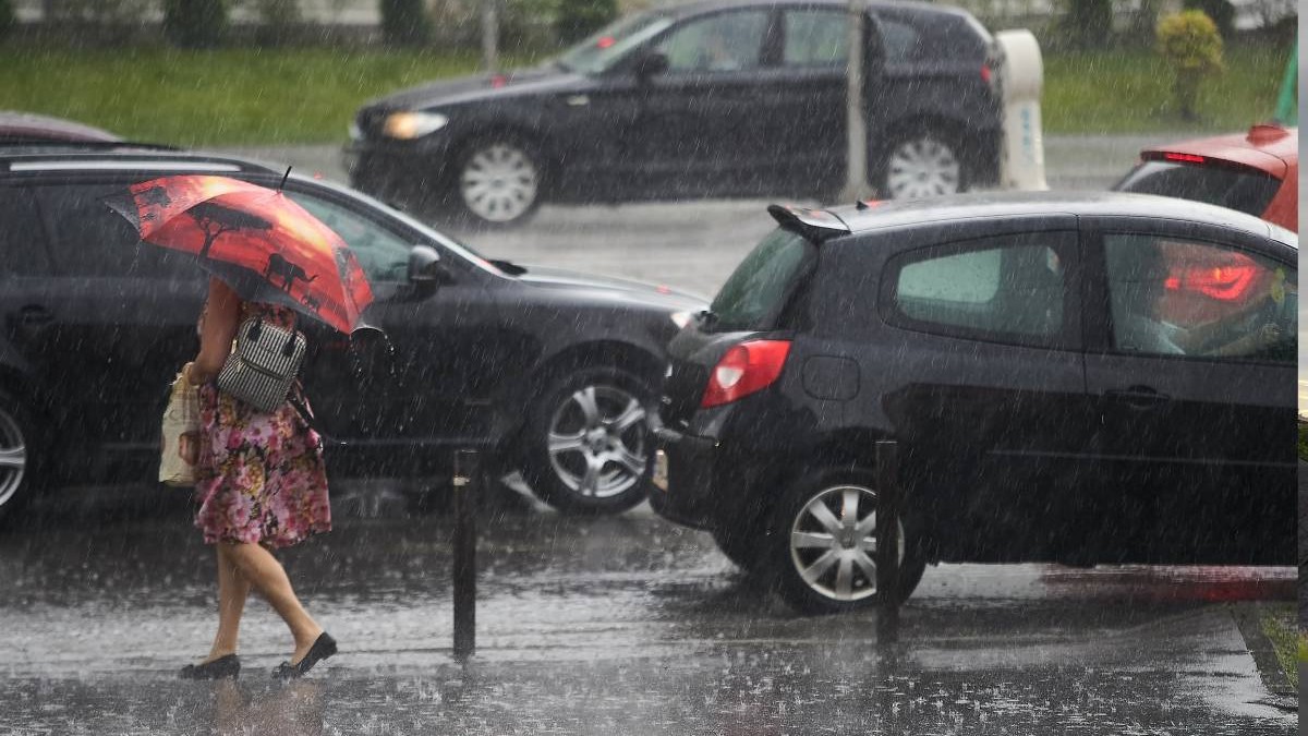 Mașinile din București blocate de o ploaie torențială de vară și o femeie în rochie, cu umbrelă, încearcă să traverseze.