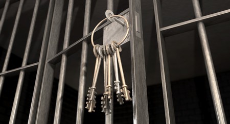 A closeup of the lock of a jail cell with iron bars and a bunch of key in the locking mechanism with the door open