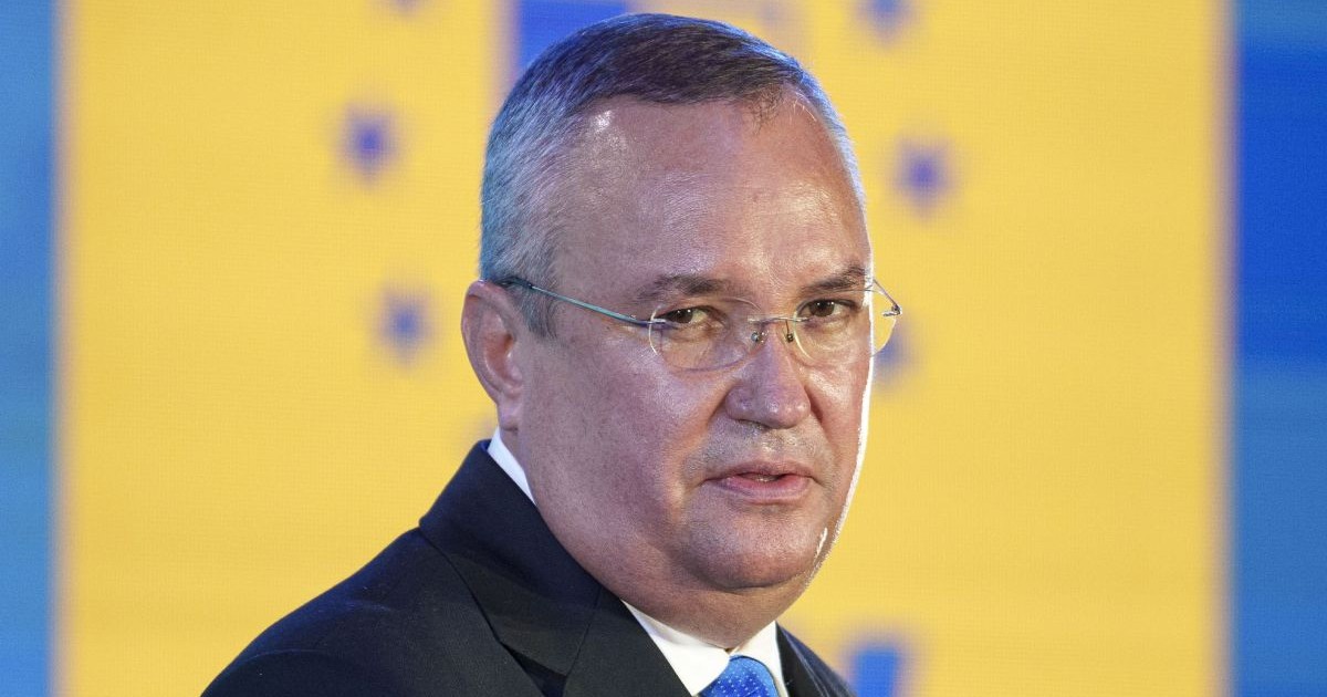 Nicolae Ciucă, îmbrăcat în costum, în prim plan, cu sigla Partidului Național Liberal pe fundal