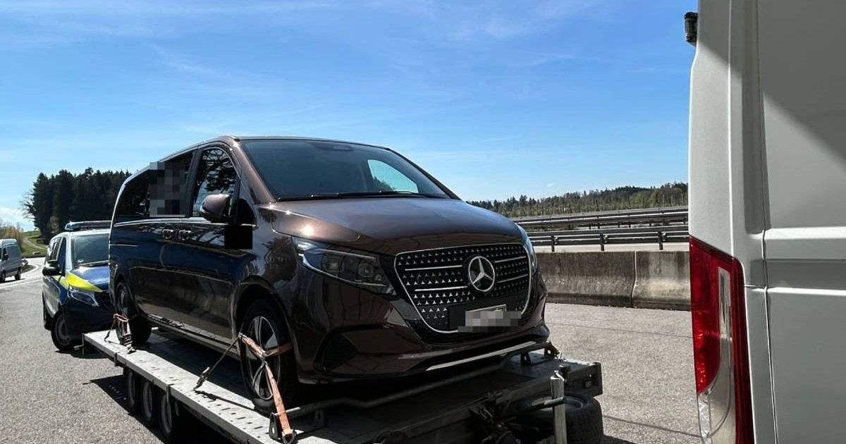 Un Mercedes V-Class negru, urcat pe o remorcă, oprit de vameși pe o autostradă, în spate se vede o masina de politie, cerul este albastru