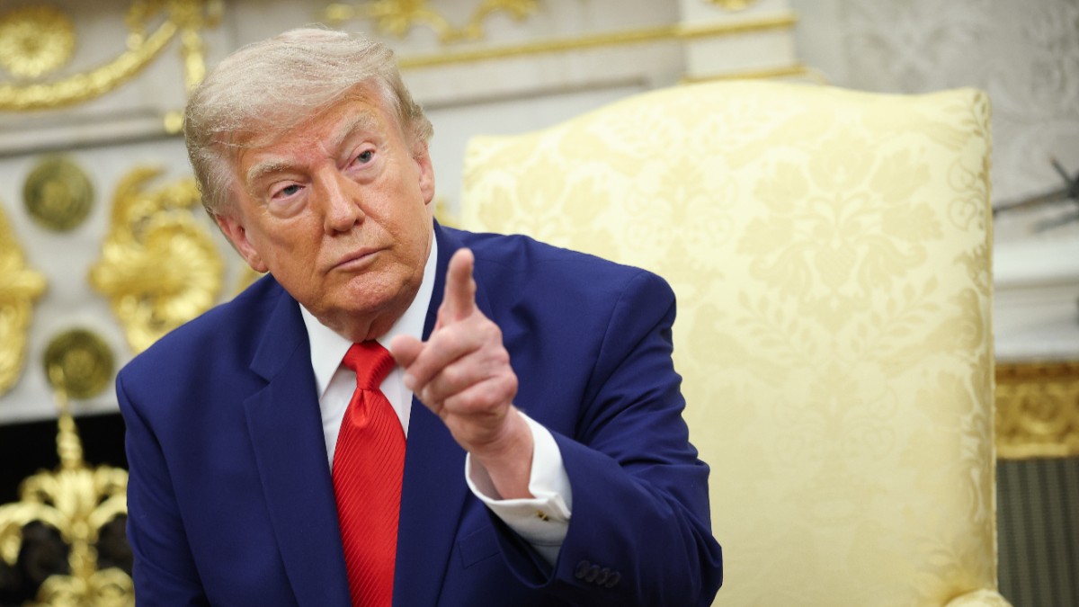 Președintele american Donald Trump, în timp ce stă pe fotoliu la Casa Albă, poartă un costum albastru și o cravată roșie și arată cu degetul spre cameră