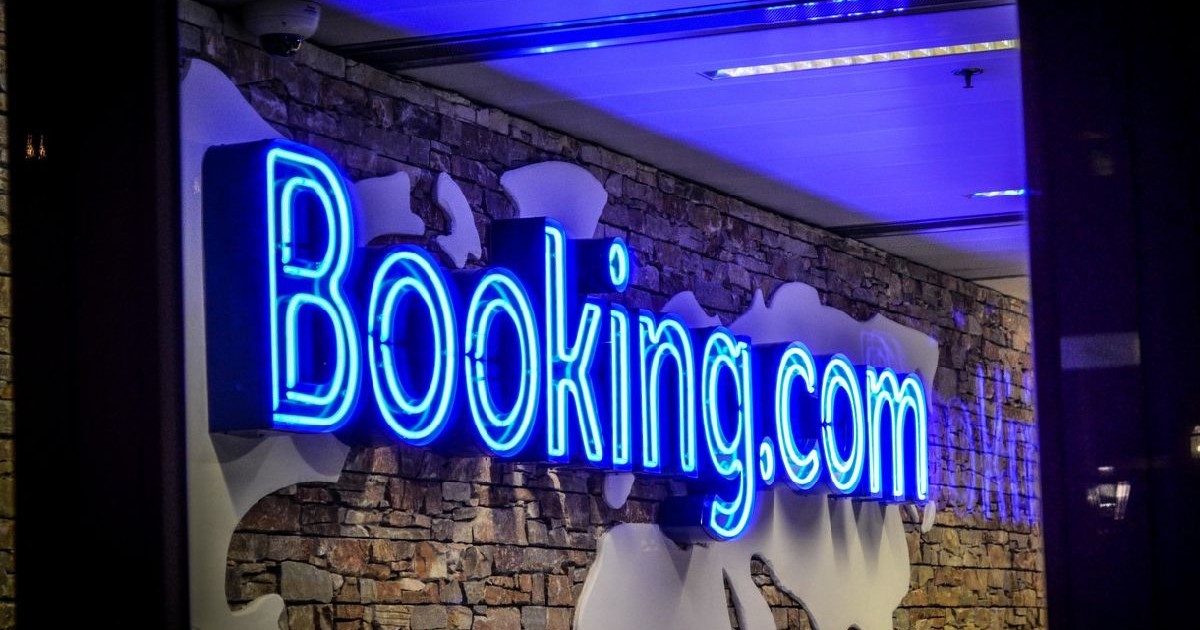 Sigla Booking.com, luminoasa in albastru, pe un perete maro, cu harta lumii in contur