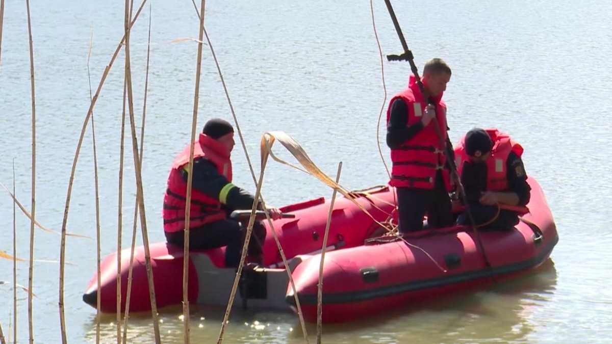 Trei salvatori într-o barcă pneumatică pe un lac, în timp ce folosesc echipamente speciale pentru a efectua o operațiune de căutare în apropierea stufului.