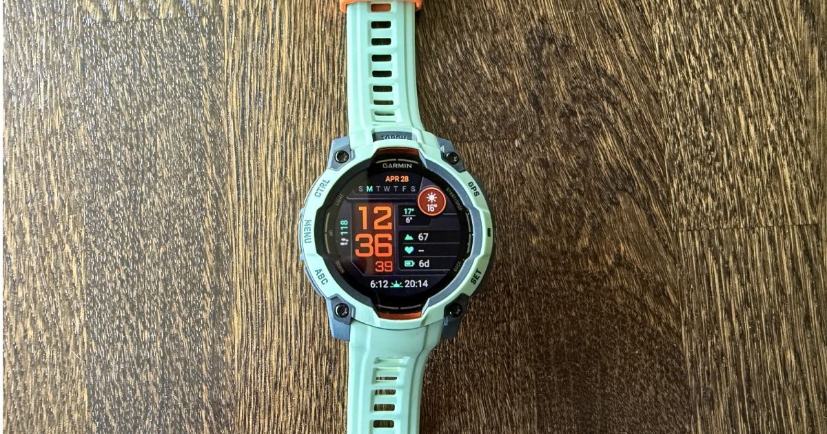 Ceas Garmin Instinct 3 AMOLED, de culoare turcoaz, așezat pe un fundal de lemn.
