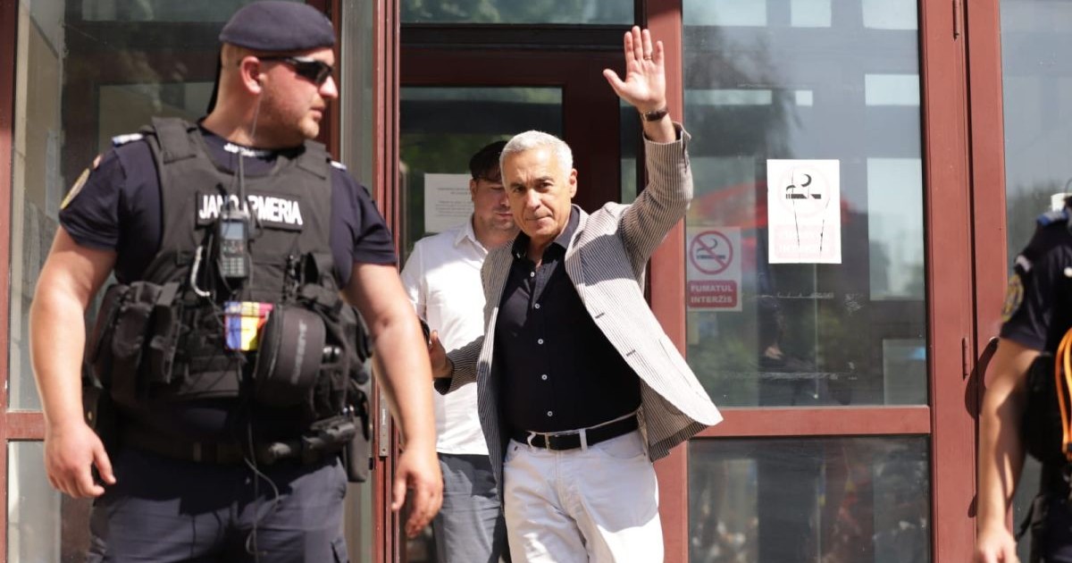 Călin Georgescu, într-un costum deschis la culoare, a ieșit de la Parchetul General și salută cu mâna stângă, în dreapta lui este un jandar, iar în spate se vede un alt bărbat, Parchetul ICCJ, București, 27 iunie 2025