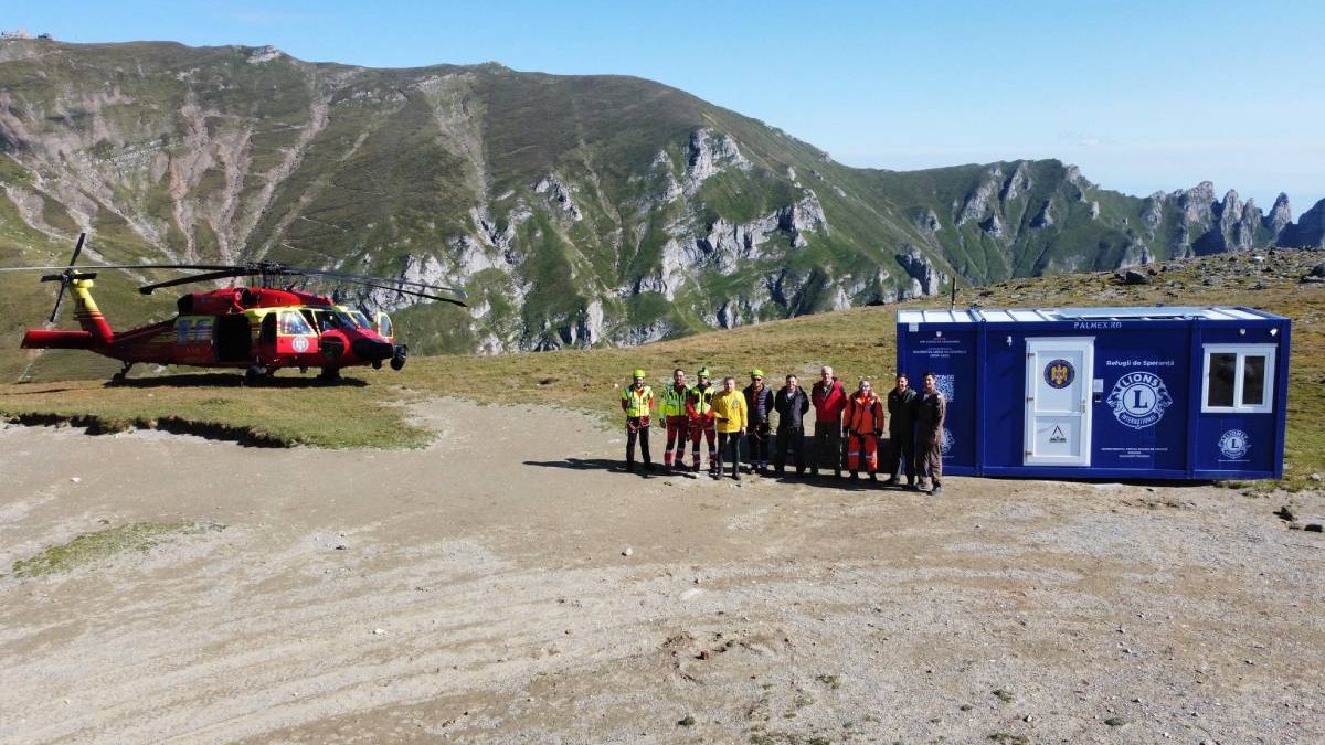 Imagine cu refugiul amplasat în Munții Bucegi. În stânga se află un elicopter, iar în dreapta se află mai mulți oameni