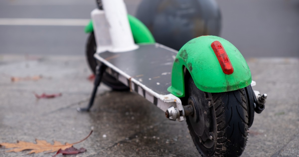 O trotinetă electrică parcată pe un trotuar umed pe care se află frunze uscate