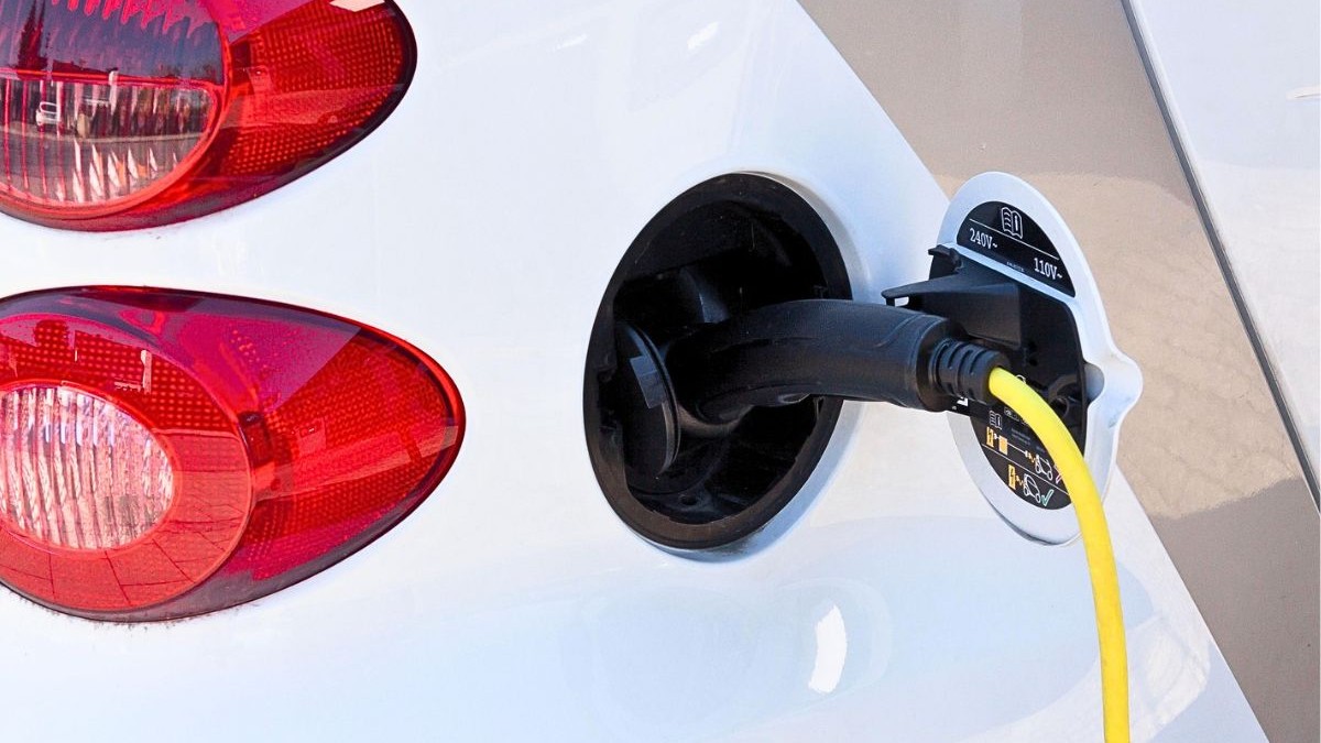 Masina electrica alba care este la incarcat de un cablu galben cu capat negru