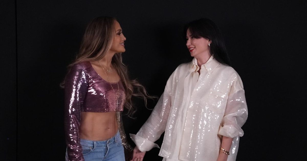 Jennifer Lopez, în stânga, îmbrăcată cu o blugi albaștri, cu talie joasă, și o bluză mov, iar Roxana Voloșeniuc, în stânga, îmbrăcată cu o bluză albă și pantaloni albi, pe fundal negru