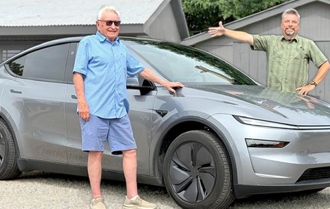 Un bărbat de 98 de ani, cu camasa albastra si pantaloni scurti albastri, langa o masina Tesla gri, pe partea opusa, un bărbat cu camasa verde