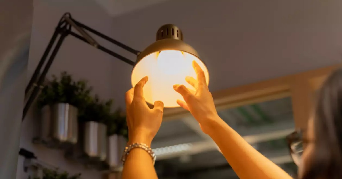 O femeie înșurubează un bec cu mâinile într-o veioză și se vede lumina
