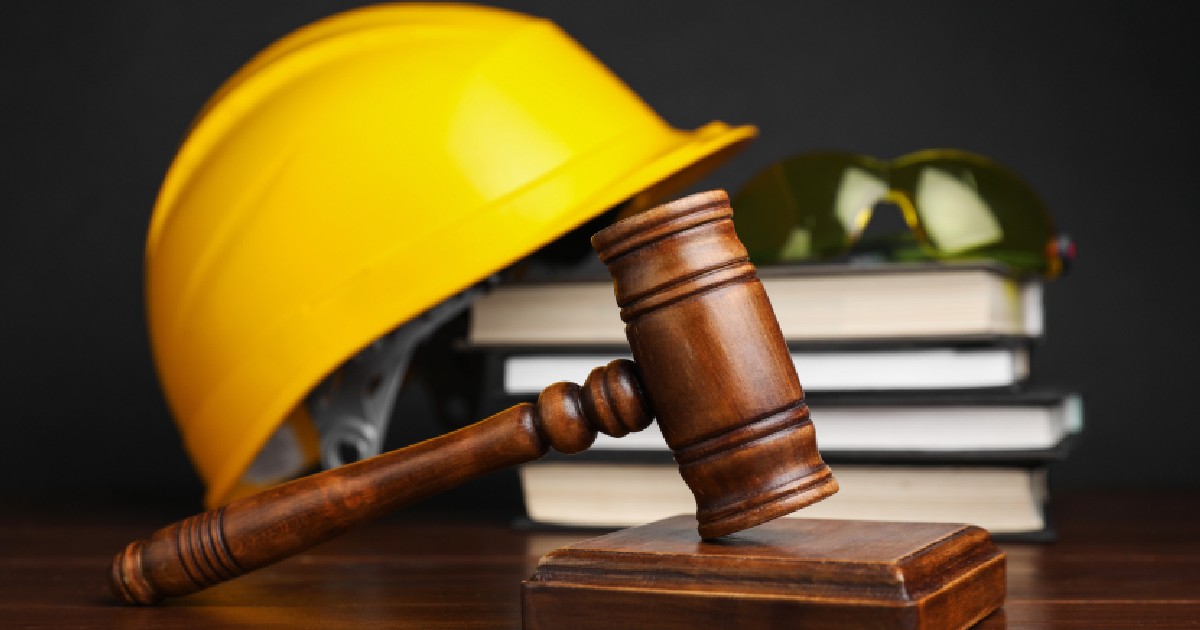 Accident de muncă: În imagine apar pe o masă din lemn un ciocan de judecător, cărți și echipament de protecție pentru muncitorii din construcții