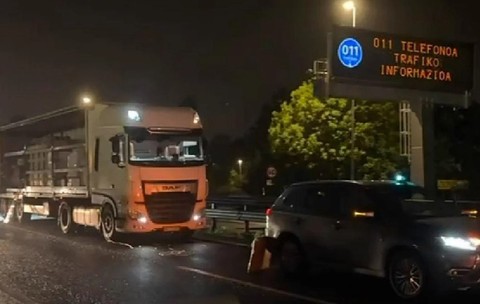 Un camion alb oprit noaptea pe marginea unui drum, alături de un alt autoturism, în apropierea unui panou electronic de informare rutieră.