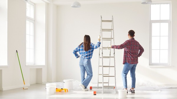 Un bărbat și o femeie priviți din spate, într-o cameră albă, aproape goală. Aceștia se află în plin proces de renovare