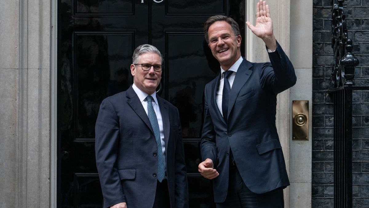 Keir Starmer, stânga, alături de Mark Rutte, cu mana stanga ridicata in semn de salut, dreapta