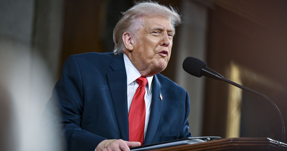 Donald Trump, cu o grimasă nervoasă, stând ușor aplecat peste un pupitru din lemn masiv, îmbrăcat într-un costum bleumarin, cu o cămașă albă și o cravată roșie