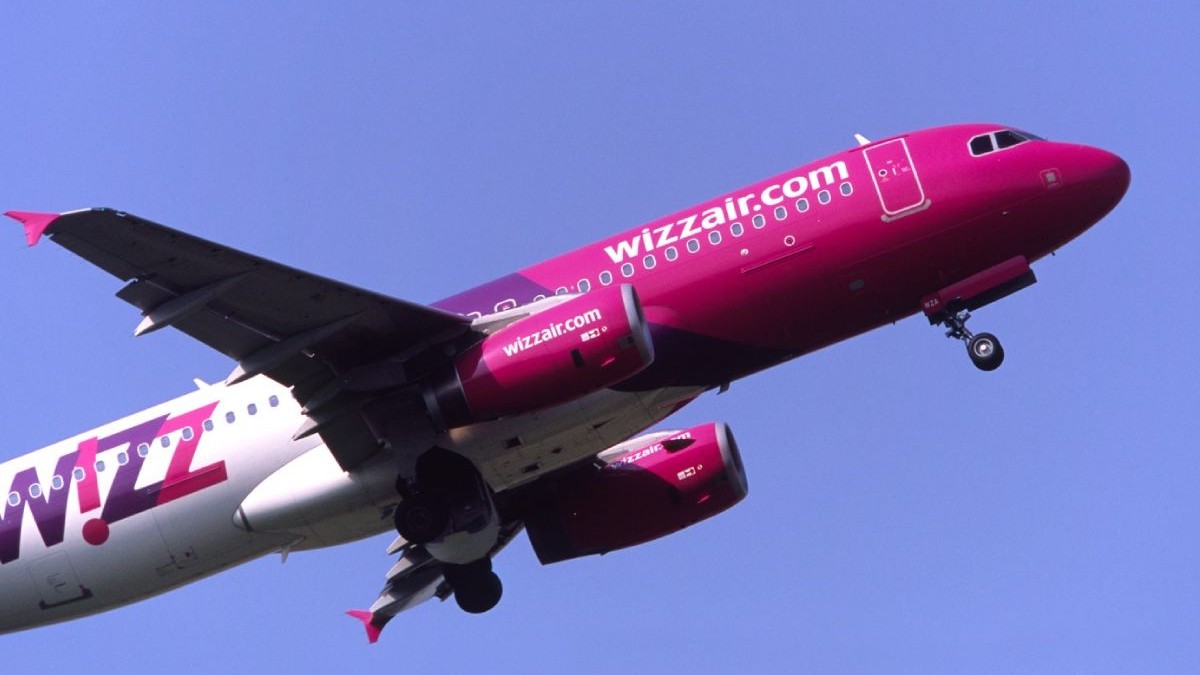 Un avion al companiei WizzAir, cu roz si alb, in zbor
