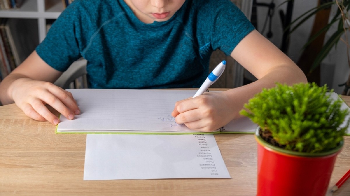 Cum faci diferența între omonime, sinonime și antonime – Un copil își face temele la limba română, scriind cuvinte noi în caiet pentru a-și îmbogăți vocabularul, exersând cuvinte și expresii