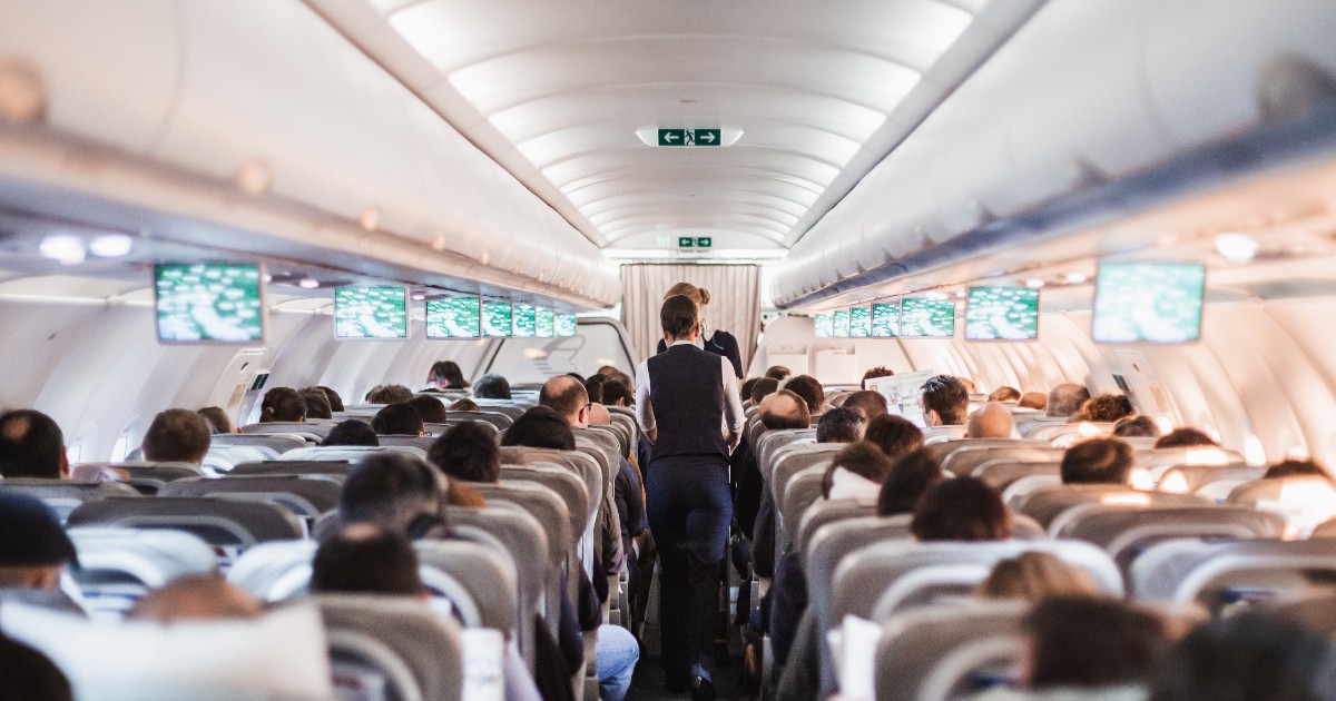 Interiorul unui avion cu pasageri așezați pe scaune și însoțitoarele de zbor pe culoarul aeronavei