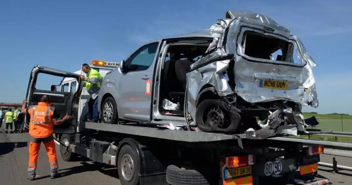 O fotografie cu o mașină argintie pe o platformă de remorcare după un accident, cu un bărbat îmbrăcat într-o jachetă portocalie care dirijează camionul.