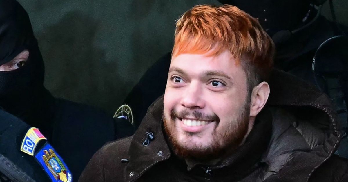 Mohamed Amra, criminalul francez prins la București, în imagine cu părul roșu și geacă neagră, ținut de un polițist mascat