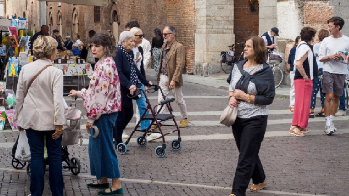 Cremona, Italia 16 septembrie 2025 Diverse grupuri de oameni, inclusiv adulți, adulți maturi și adulți în vârstă, mersul pe jos și cumpărăturile la o piață stradală vibrantă pe o stradă pietruită