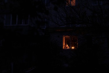 Caterina, o femeie în vârstă de 70 de ani, se uită pe fereastră, în timp ce ține o lumânare aprinsă în casă, în timpul unei pene de curent, în Borodianka, regiunea Kiev, pe 20 octombrie 2022 | Foto: Profimedia