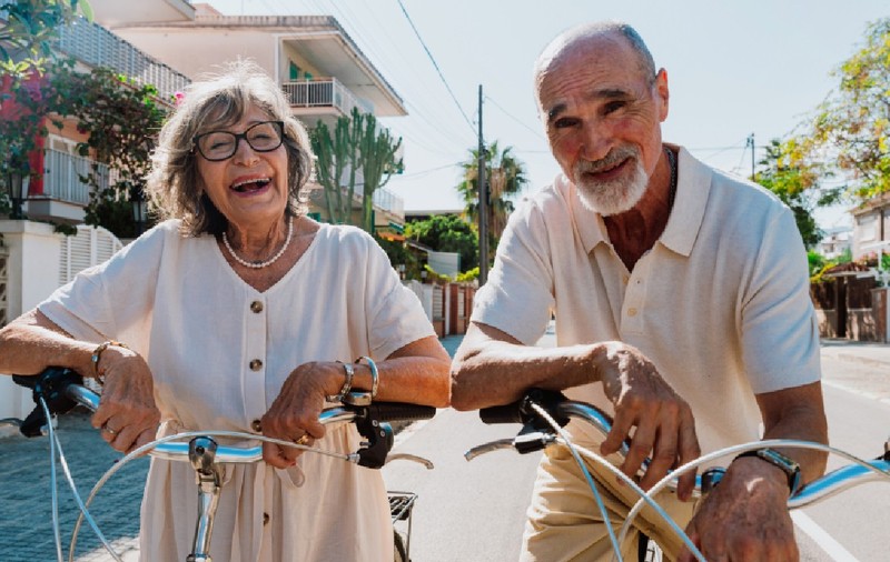 Cuplu senior fericit plimbându-se cu bicicleta în aer liber, zâmbind