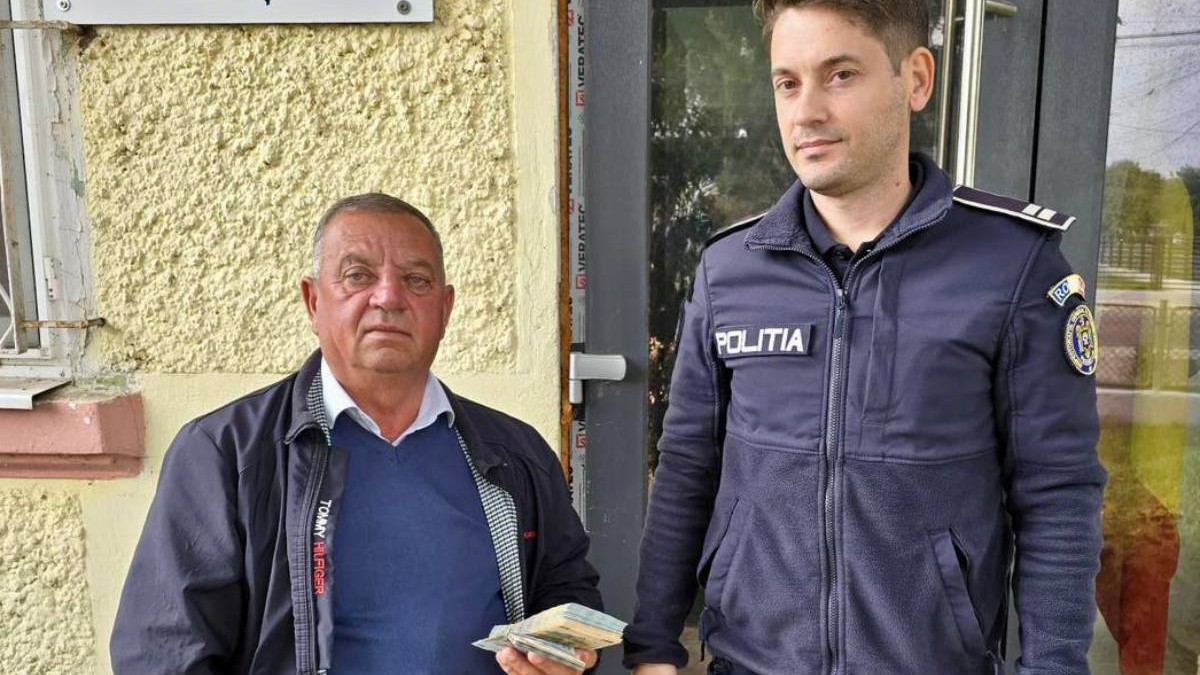 Un polițist din județul Vrancea, alături de un bărbat din Vrancea care ține în mână un teanc de bani, bancnote de câte 100 și 200 de lei, fotografiați în fața Secției de Poliție