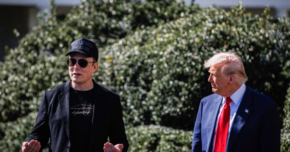 Elon Musk, îmbrăcat în negru, cu șapcă și ochelari, gesticulează, în stânga lui, este Donald Trump, în costum albastru, cămașă albă și cravată roșie, care îl privește - martie 2025