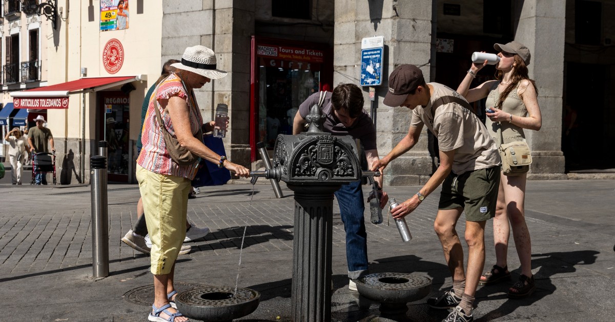 Mai mulți oameni care încearcă să se răcorească și iau apă în sticle de la o fântână stradală
