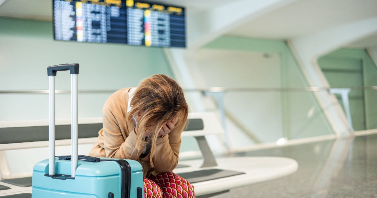 O femeie care stă pe scaun în aeroport, cu valiza lângă ea, supărată după ce a pierdut o vacanță