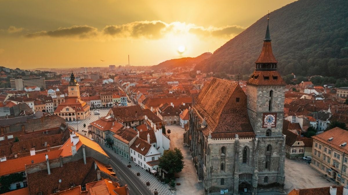 Aerial drone view of the The Black Church in old Brasov centre at sunset, Romania. Old residential buildings around it, hills with greenery