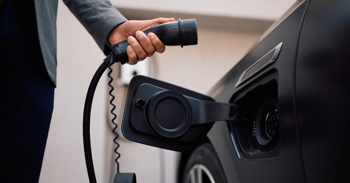 Un bărbat îmbrăcat în negru, în timp ce pune o mașină electrică la încărcat