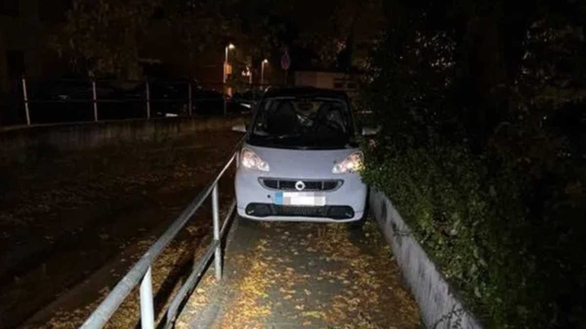 Un smart de culoare alba, blocat pe un trotuar ingust plin de frunze galbene, noaptea, Austria