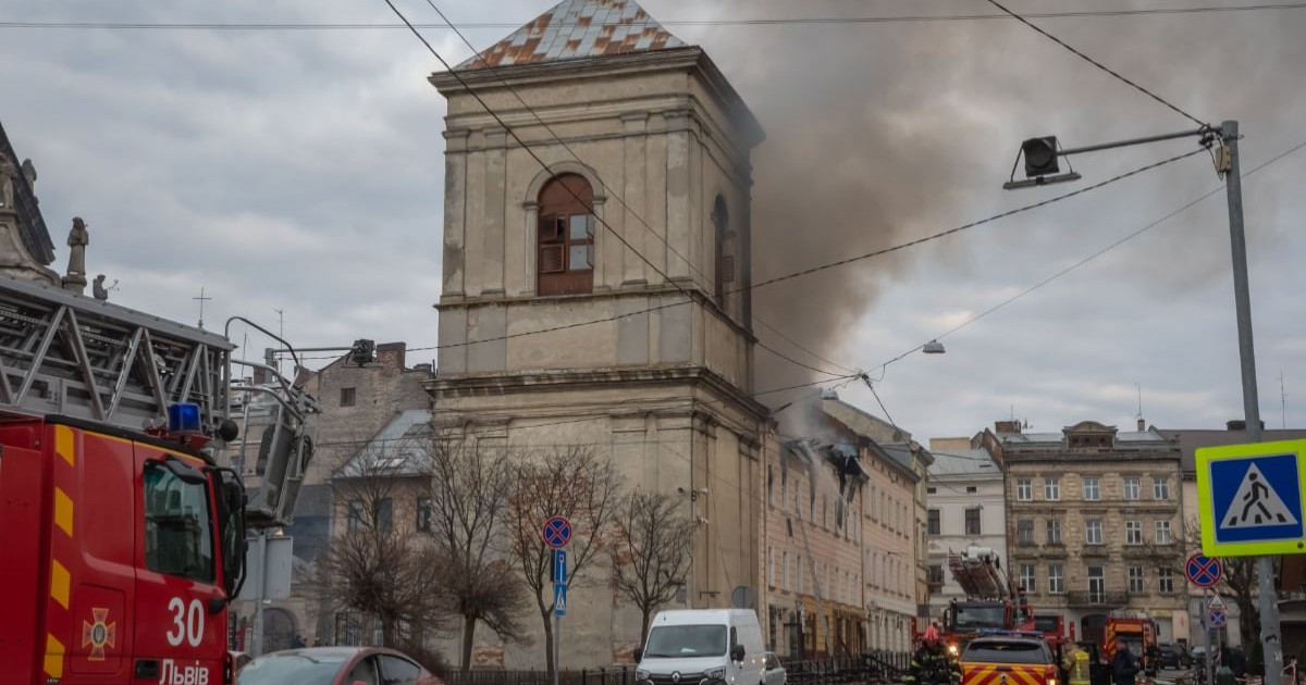 Pompieri care intervin la un incendiu într-o clădire istorică, cu fum gros ieșind de pe acoperiș.